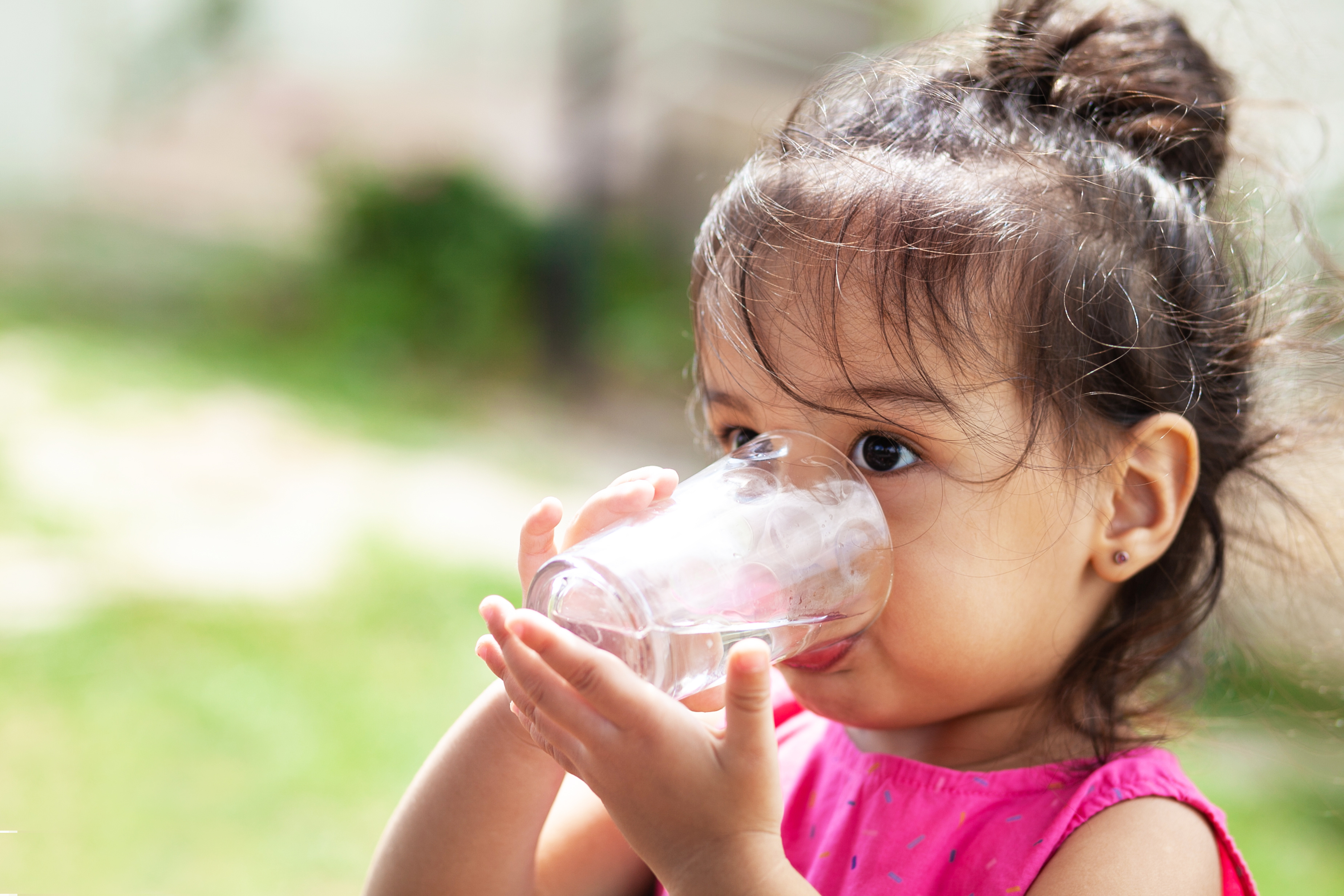 Preschool age child with light brown skin and dark brown hair drinking a glass of water