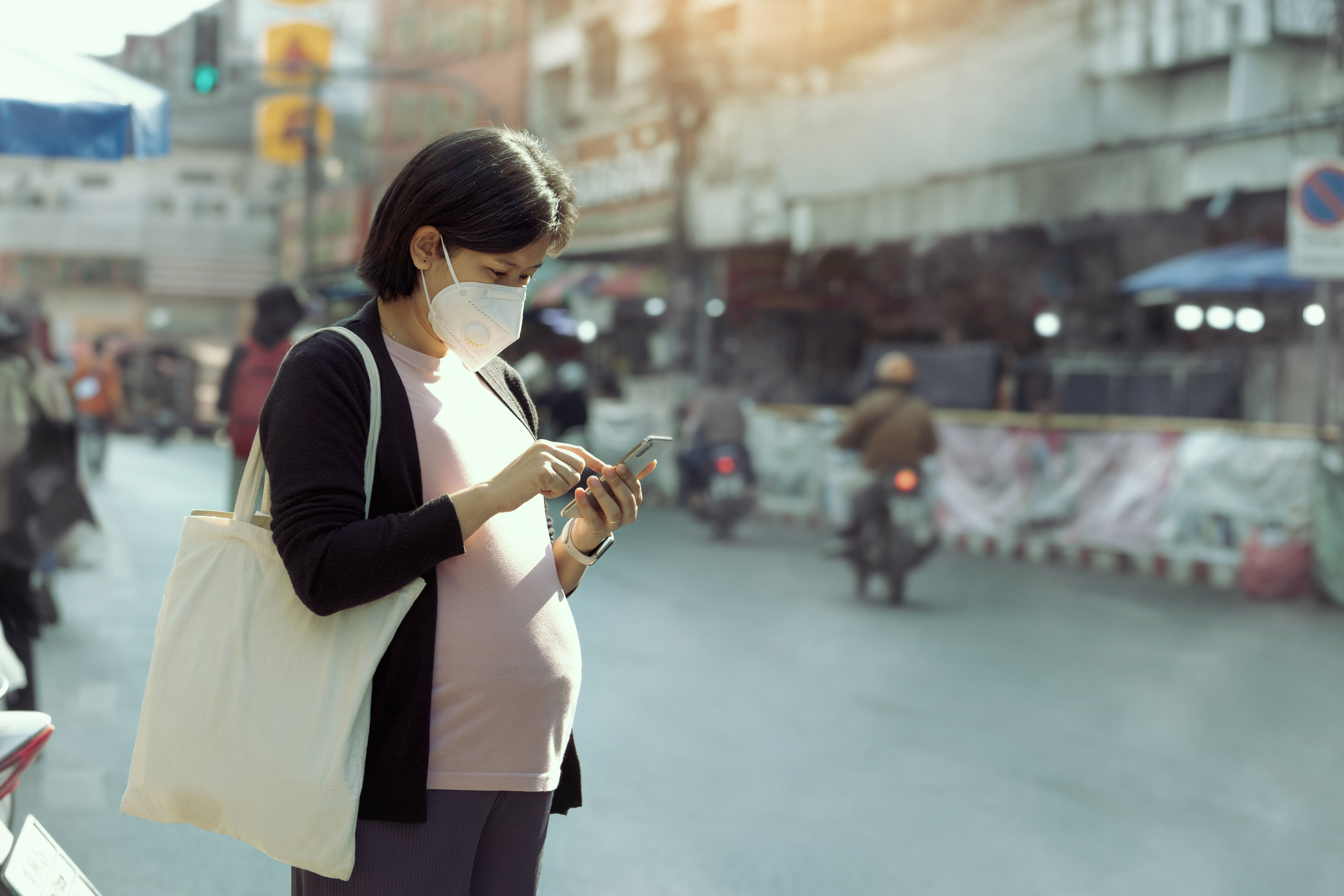Pregnant person standing in a city landscape with visibly polluted air, wearing a mask