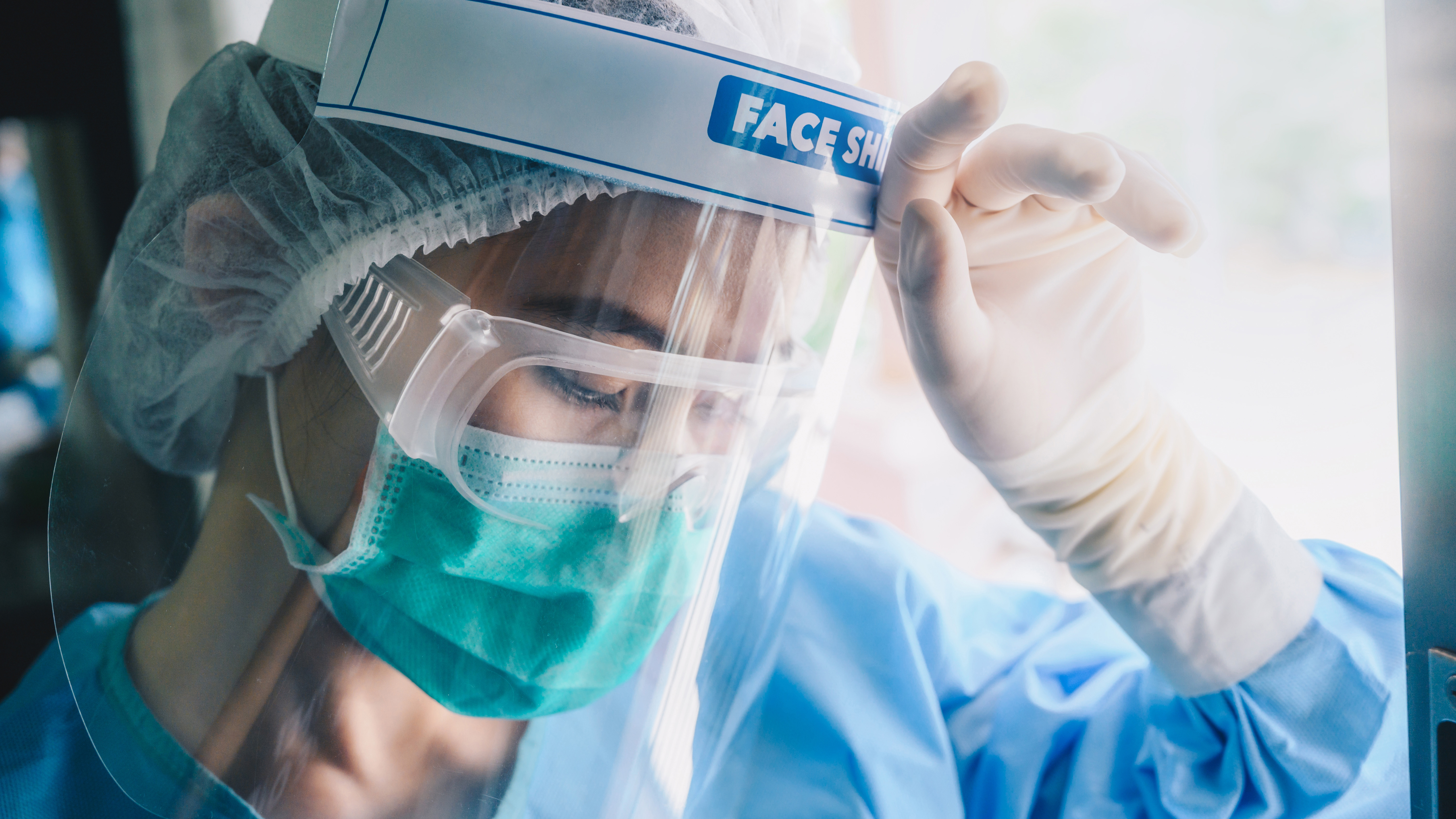 Image of healthcare worker with a face shield and mask, looking exhausted 