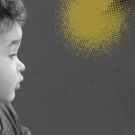 Black-and-white photo of a toddler in profile looking out a rain-covered window with yellow and black dots representing pollution.