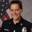 Smiling woman in a firefighter uniform with an American flag backdrop.