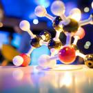 Glossy molecular model of DNA with connected colored spheres, blurred colorful background.